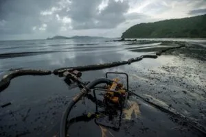 Lupa Ambiental | Equipamento skimmer e barreiras de contenção em praia com areia e água contaminadas por óleo.