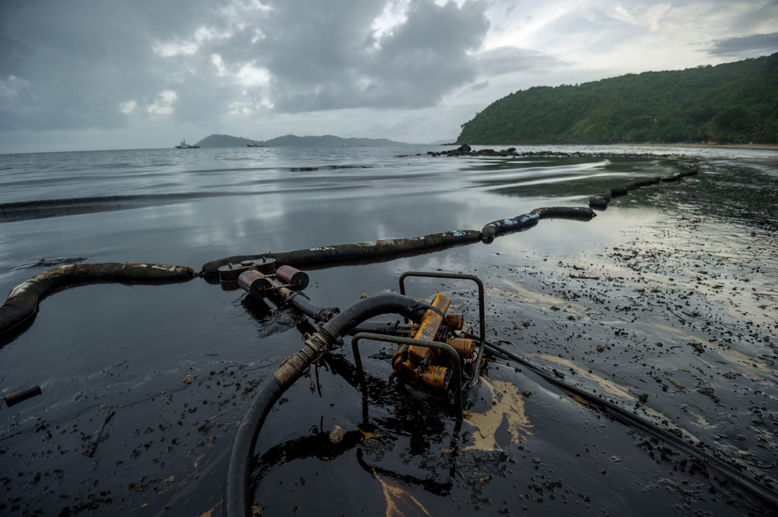 Lupa Ambiental | Equipamento skimmer e barreiras de contenção em praia com areia e água contaminadas por óleo.